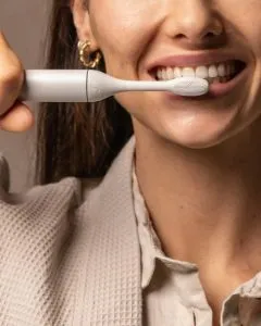 a woman brushing her teeth with an eco-friendly toothbrush