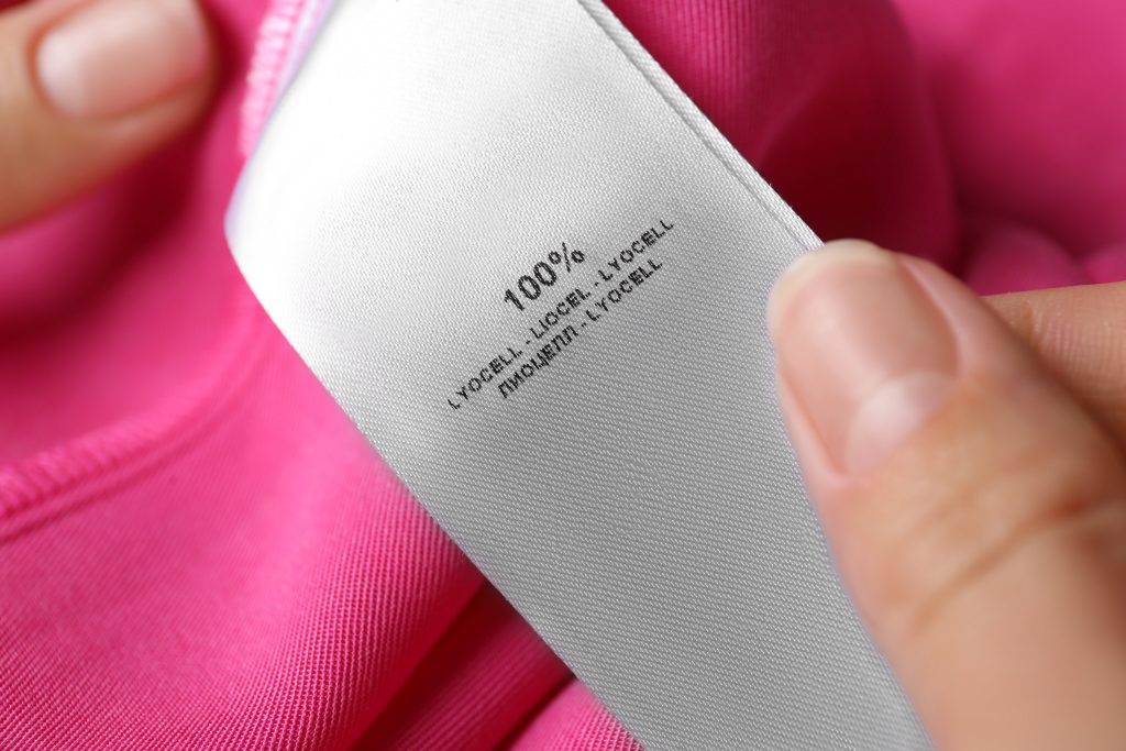 Woman reading clothing label with material content on pink shirt, closeup, 100% lyocell