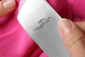 Woman reading clothing label with material content on pink shirt, closeup, 100% lyocell